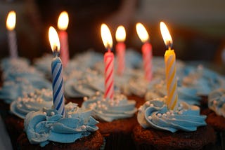 Cupcakes with blue swirled frosting and colourful lit birthday candles