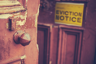 Image description: Broken, old-fashioned door with chipped paint has a yellow sign reading “Eviction Notice” on it. Title: Supreme Court’s decision to block eviction moratorium amid COVID-19 surge will be a public health disaster. Keywords: Supreme Court, eviction moratorium, COVID-19, pandemic, public health, coronavirus