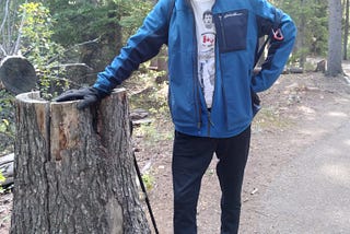 A smiling elderly Al, Jr. in the setting he enjoyed most — nature — leaning on a tree stump.