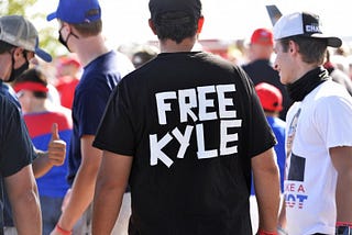A group of white men gather together with one man wearing a black shirt that spells out “Free Kyle” on the back