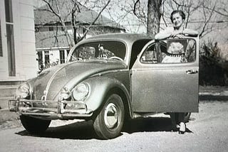 Black and white photo of a car with a woman standing by the open door