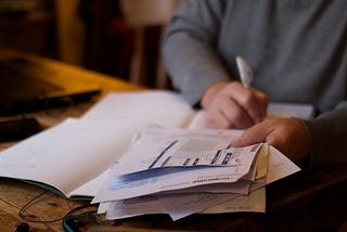 A man sits with a pen editing a large stack of papers