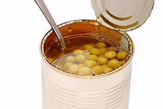 Photo of an open can of green peas with a spoon in it.