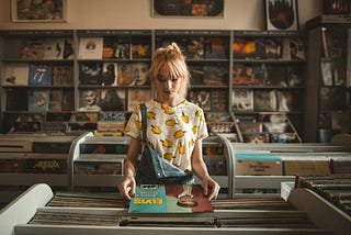 A woman standing in a record store looking at an Elvis record