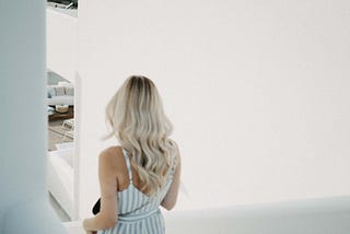 Blonde woman in a blue and white sun dress walking down stairs into a mostly obscured living room.