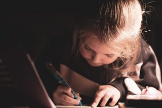 A young girl poised with a pen over a notebook, presumably completing her homework