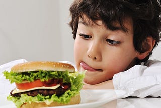 A boy looks longingly at a burger, he slicks his lips, ready to eat, I have had the burger, Tim’s Grateful 8
