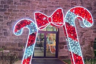 2 giant candy canes with a giant bow in the middle made from fairy lights outside the entrance to a building
