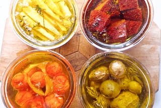 four jars of oil and confit’d veg — parsnip, beet, tomato, and potatoes — in rich color