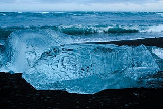 Clear, almost blue ice on black sand near the ocean