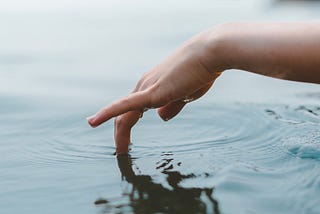 Arm hanging out of a small boat, with fingers dipping into water.