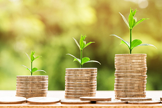 3 stacks of coins: short on left, medium height in middle, tall on right, each with leaves growing from them.