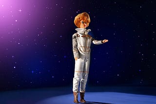 Vintage Barbie doll in a silver spacesuit is standing in front of a pink and blue galaxy background. The doll has short curly hair and an arm is outstretched as if to point to something