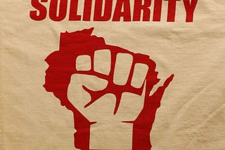 Solidarity written in red script on brown paper, with a red fist held up in the sky