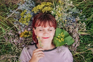 Women laying on grass smiling with flowers around her head.