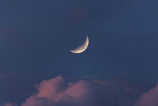 a quarter moon in the middle of a dark blue night sky with pink clouds puffing down below