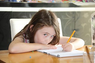 Young girl writing while giving the viewer a side-eye. She looks confident. Creativity. Flow state. Writing.