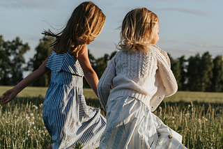 two little girls running in a field of grass