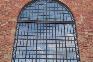 A large red brick wall with a large window with a arched top and a bicycle in front.