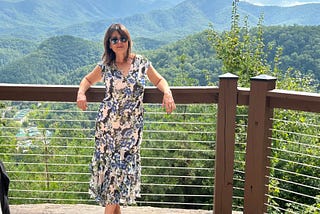 Picture of author wearing a nice dress and sunglasses in front a a spectacular view of the smokey mountains. Subject looks fancy because she is at a wedding — she looks confident with a slight smile and attitude.