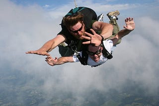 Two people tandem skydiving with Earth visible below clouds