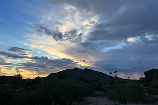 White clouds are scattered across a blue and orange just-after-sunset sky. A dark mountain sits beneath.