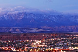 The metropolitan area of St. George, Utah (population 208,000 in 2024). The cloud-covered Pine Valley Mountains are in the background and low-rise buildings in the foreground. Photo by St. George Chamber of Commerce on Wikipedia here.