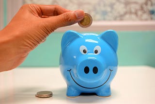 Someone putting coins into a blue smiley biggy bank.