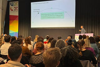 A speaker at UXLx presents a slide titled “AI Design Pattern Framework” to a seated audience.