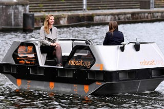A view of the Roboat Watertaxi with two passengers on a waterway.