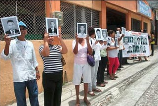 Family members of the youths who were victims of the “false positives scandal” in Colombia protest in the street while holding photographs and placards with their faces and names.