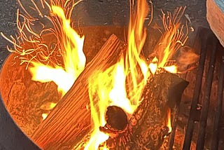 Bright yellow and orange flames dance around fresh logs on a campfire.
