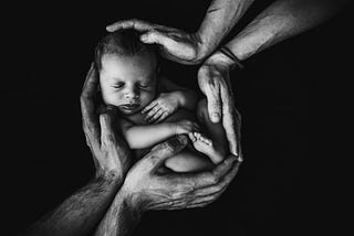Four hands cradling newborn.