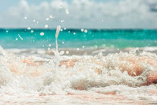 white foam ocean waves wash over pink sand beach