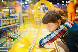 Young child looks longingly at Lego display behind glass.