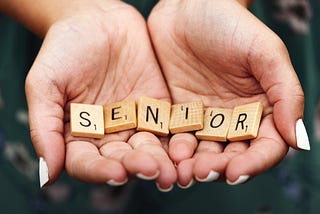 Macro shot of teen girl with manicured fingernails holding scrabble letters spelling the word “SENIOR” in the palms of her cupped hands.