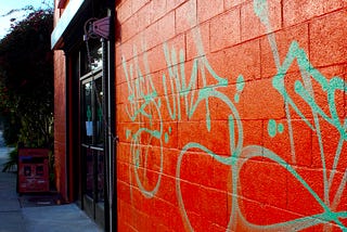 A bright red-orange cement brick wall with turquoise graffitti