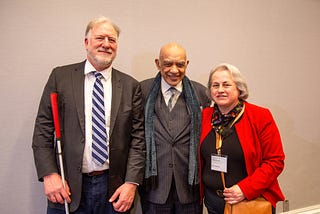 Two men and a woman stand side by side smiling.