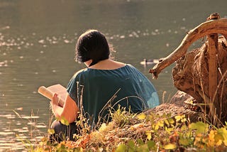 how to find the healer within cover image — a girl with a dark hair and a teal shirt sitting by the water peacefully with a book in her hand