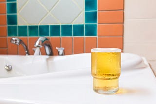 A glass of beer placed on a surface near a running tap.