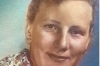 Colourised head and shoulders studio portrait of a young white woman (Elli Immo). The woman is looking into the camera and smiling slightly. Photo has been taken by Kemin Kuvaamo photo studio.