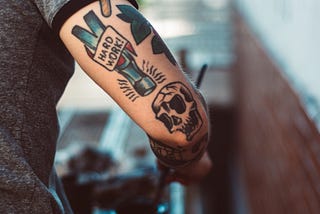 Tattoos on the back of an arm. The words “hard work” appear on a hammer with a skull underneath.