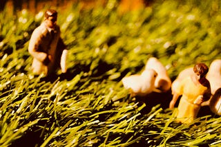 Small plastic models (of a man, a woman and some chicks) walk through long grass.