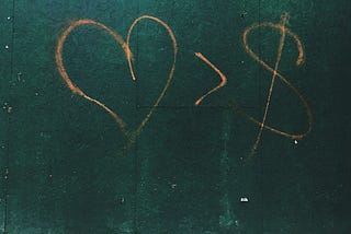 Graffiti on a wall showing a heart in preference to a dollar sign.