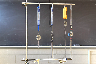 The image shows 4 sets of springs connected together and mounted vertically with a 50 gram mass in the middle
