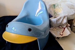 A blue plastic baby potty sits in front of a pile of disposable diapers and a reusable one.