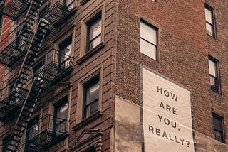 Picture of a brick building with a sign that says ‘How are you, really?’