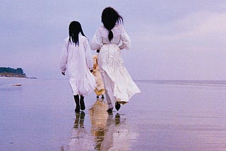 Three women dressed in white and cream dresses walking along a beach.