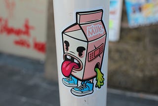 A sticker with a cartoon of a carton of milk with a face sticking its tongue out.