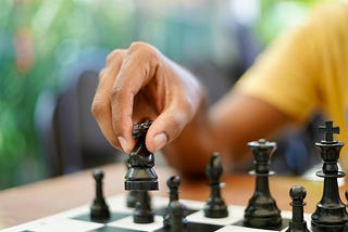 A person’s hand moves a chess piece across a chess board
